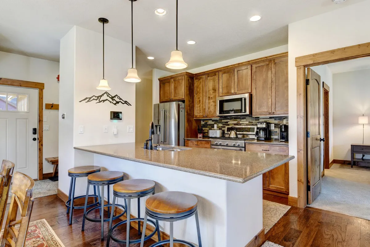 A bright, spacious kitchen featuring a central island with bar stools, modern appliances, and warm wooden cabinetry. The island provides ample prep space and a natural spot for casual breakfasts or chatting while meals are prepared. The inviting setup hints at both gourmet cooking and family gatherings.