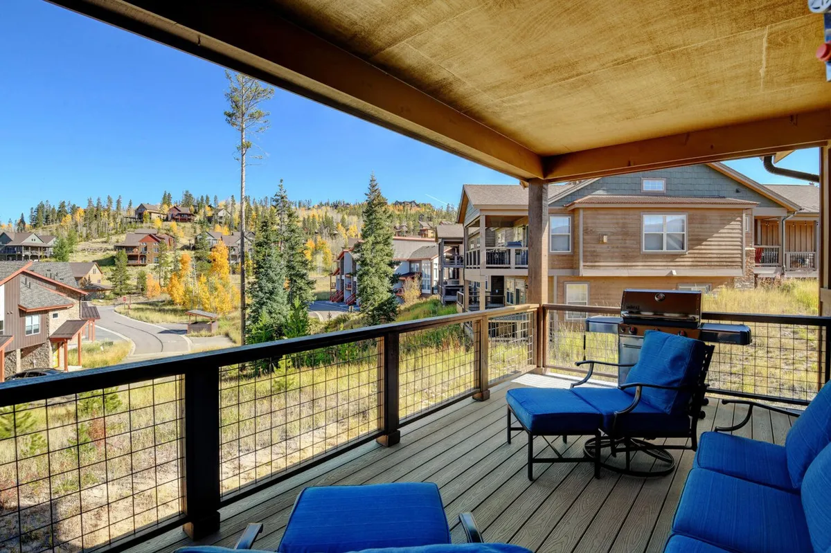 An inviting exterior deck with comfortable furniture facing panoramic mountain views and surrounded by trees. The space is perfect for relaxing, dining, or enjoying the natural beauty of the area.