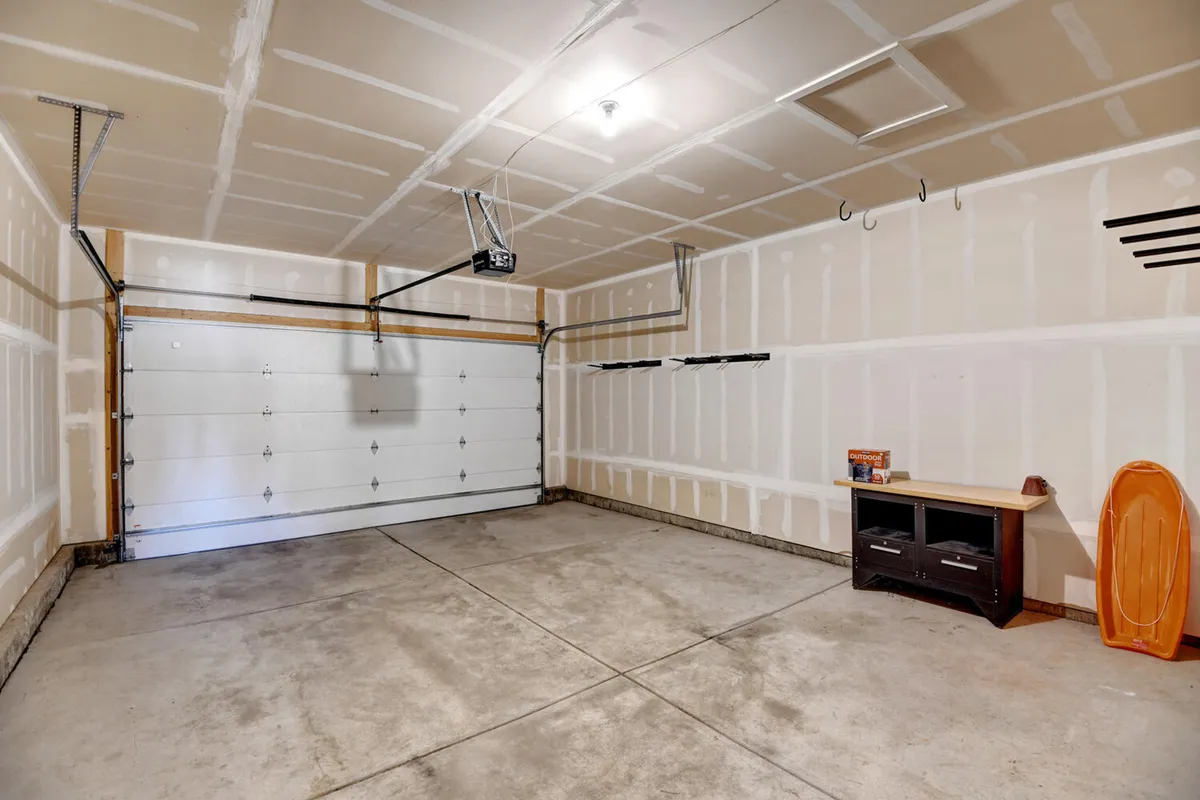 An interior look at a spacious garage featuring a garage door, workbench, and sled. The organized layout highlights practical storage space for vehicles and recreational gear, making it ideal for adventure enthusiasts.
