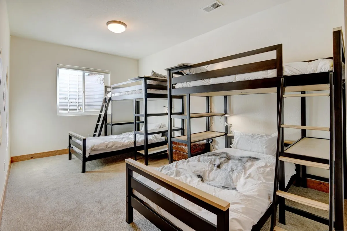 A cheerful bunk bedroom featuring sturdy bunk beds, a window with sunlight streaming in, and warm flooring. The room feels playful and welcoming, ideal for children or families.