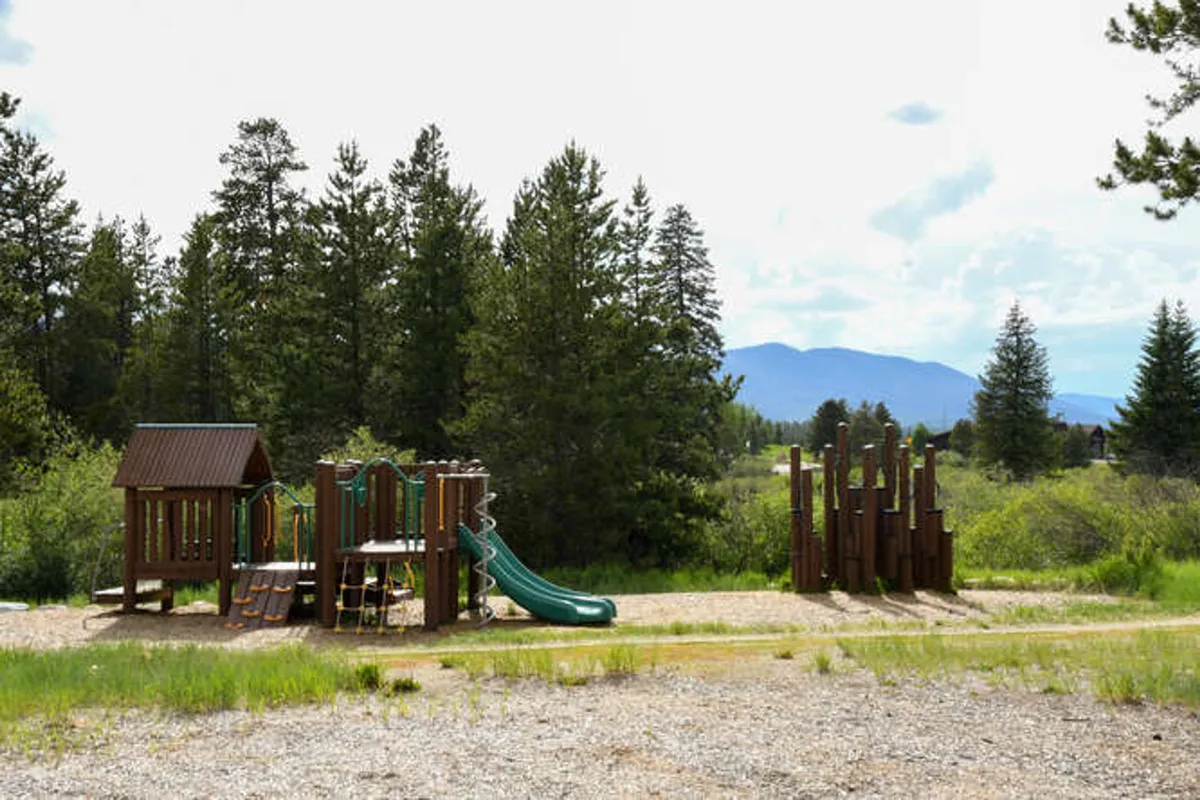 This image features a vibrant playground structure with slides and climbing features set outdoors, inviting children to play while families enjoy picnicking and gathering in the surrounding green space. The mood is joyful and adventurous, capturing the spirit of family fun and outdoor recreation.